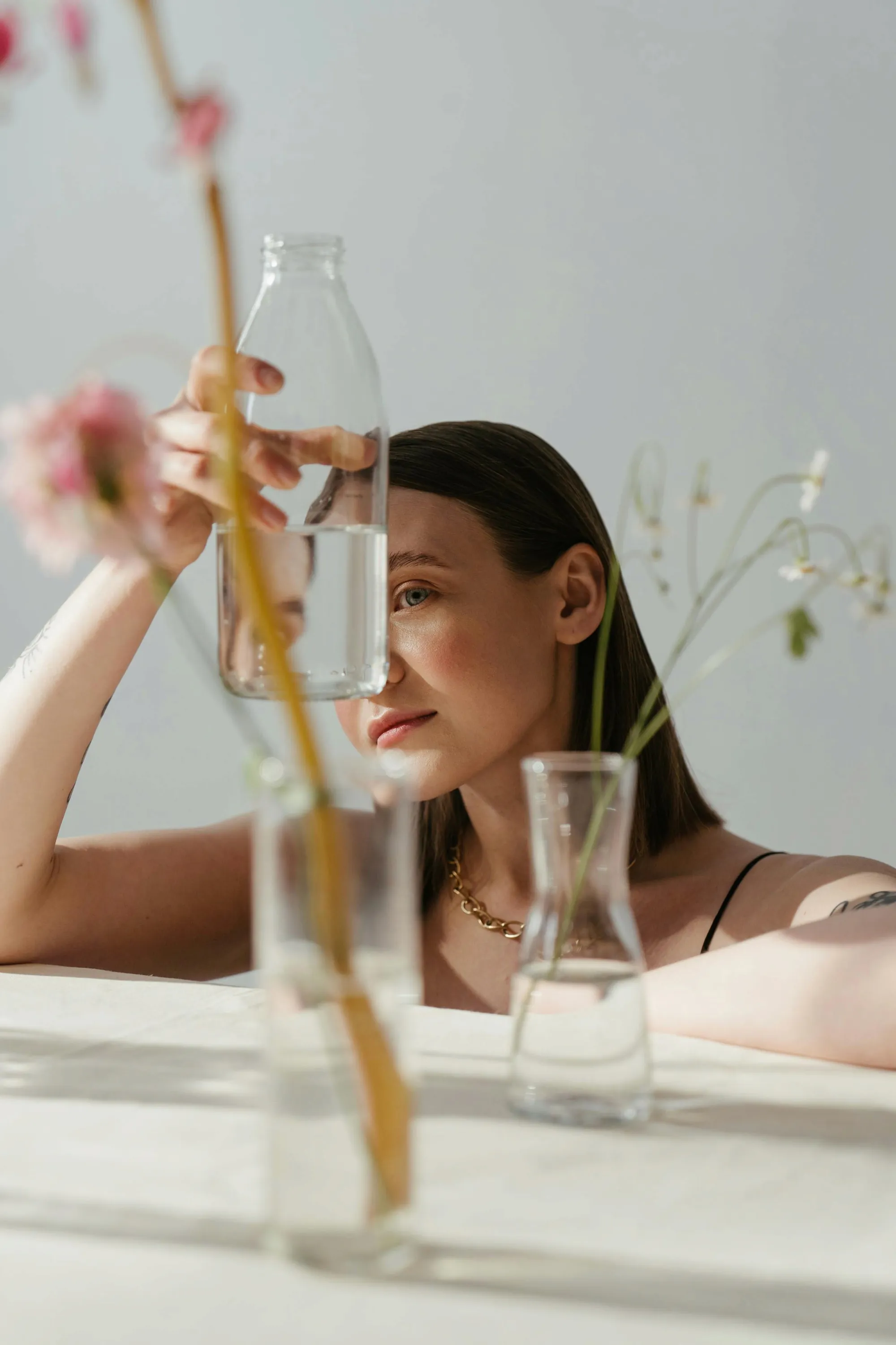 A woman resting her head behind glass vases of pink flowers